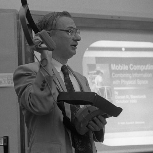 An image of a man holding a headset, standing in front of a projector image which says "Mobile Computing"